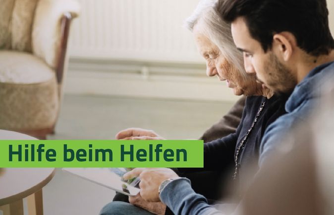 Junger Helfer zeigt ältere Frau Tablet mit Schriftzug Hilfe beim Helfen