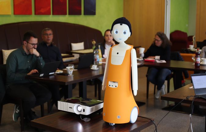 Sozialroboter Lucki mit orangefarbenem Körper vor Meetingteilnehmenden