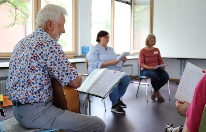 Älterer Mann spielt Gitarre in kleiner Sing- und Gesprächsrunde beim Informationsabend