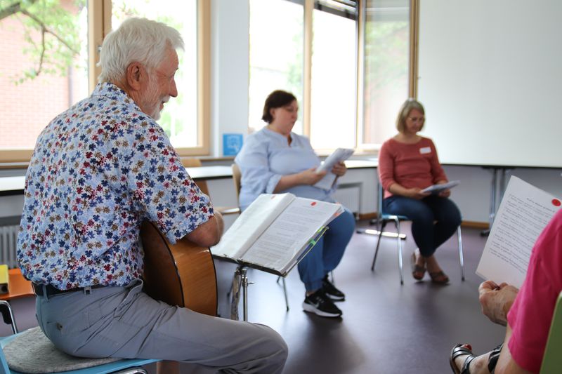 Älterer Mann spielt Gitarre in kleiner Sing- und Gesprächsrunde beim Informationsabend