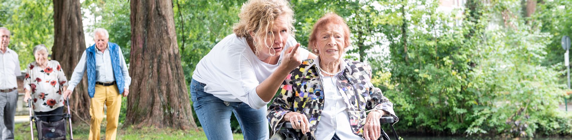 Pflegekraft zeigt der älteren Frau im Rollstuhl etwas im Park
