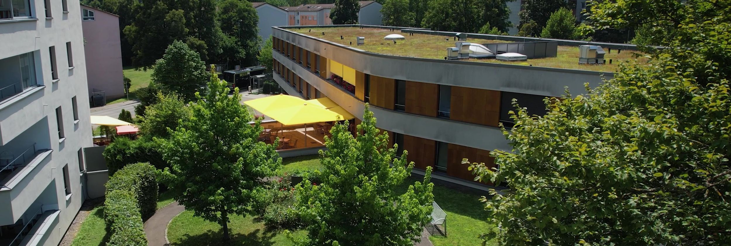 Innenhof mit Bäumen, Wegen und gelben Sonnenschirmen zwischen Wohnhäusern